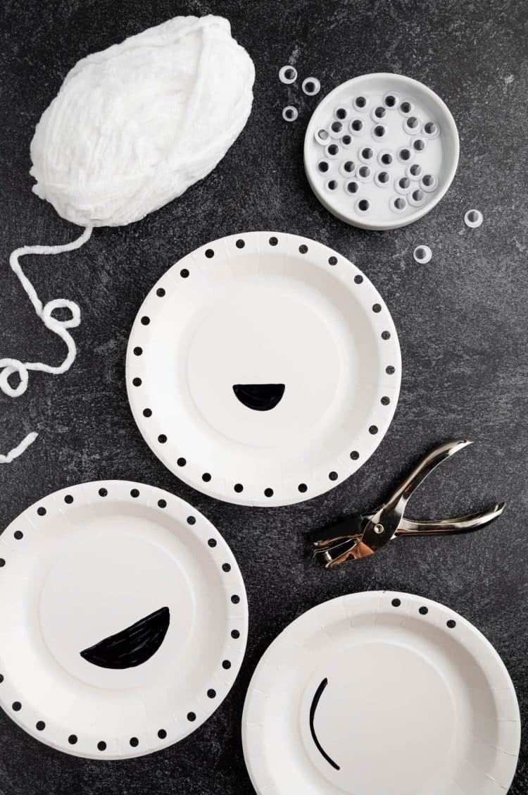 Paper plates with mouths cut out from them and holes punched around circumference of plate
