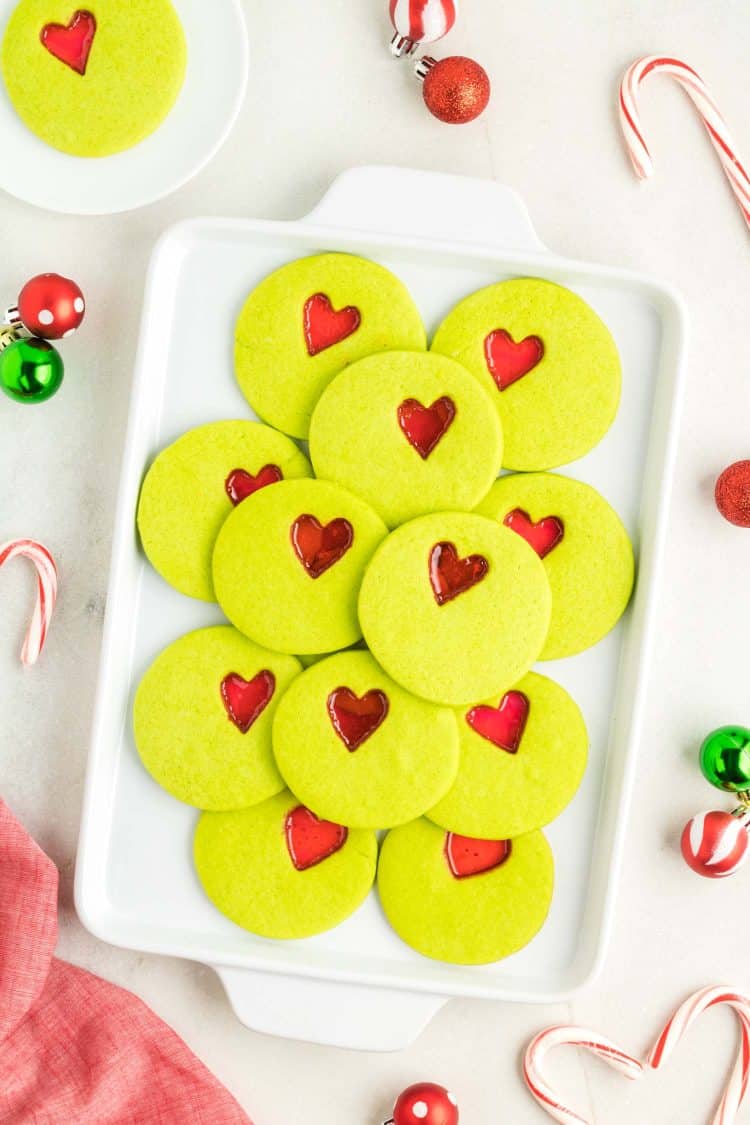 Stack of Grinch Christmas cookies on platter with candy cane and holiday ball background