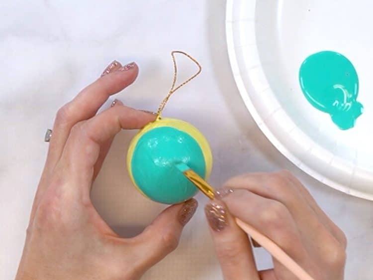 Close up of hands painting a round Christmas ornament with aqua paint