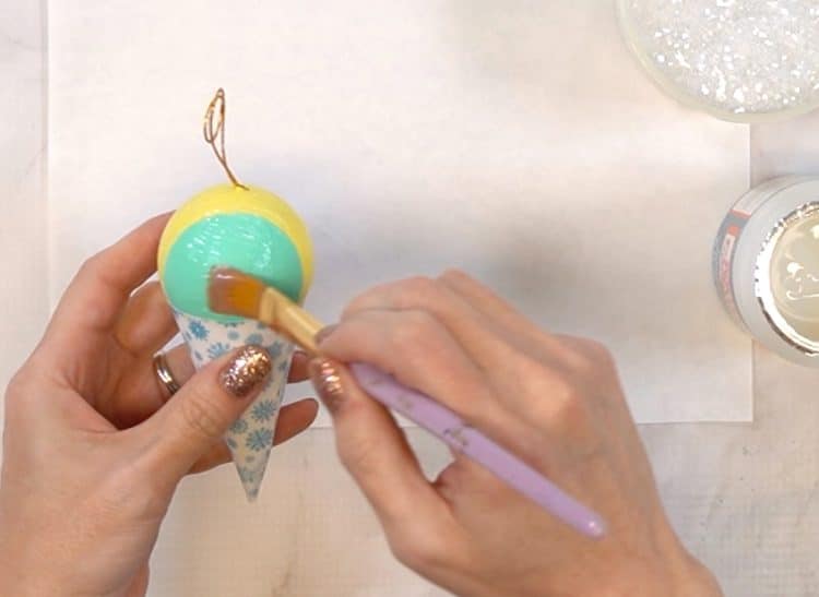 Painting a coat of glossy Mod Podge on to a snow cone ornament in preparation for glitter