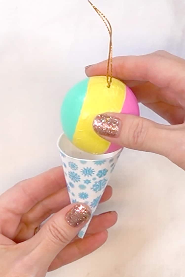 Close-up on hands gluing a painted round Christmas ornament on top of a paper cone