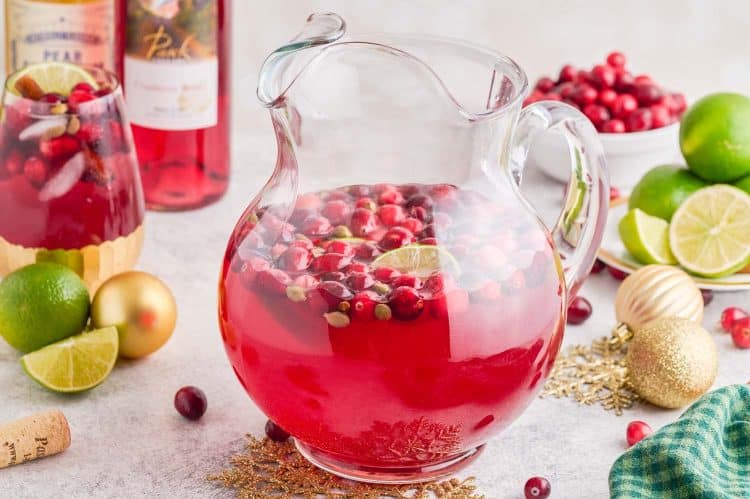 Glass pitcher of Spiced Cranberry Wine Spritzer with cranberries floating in it, on a table