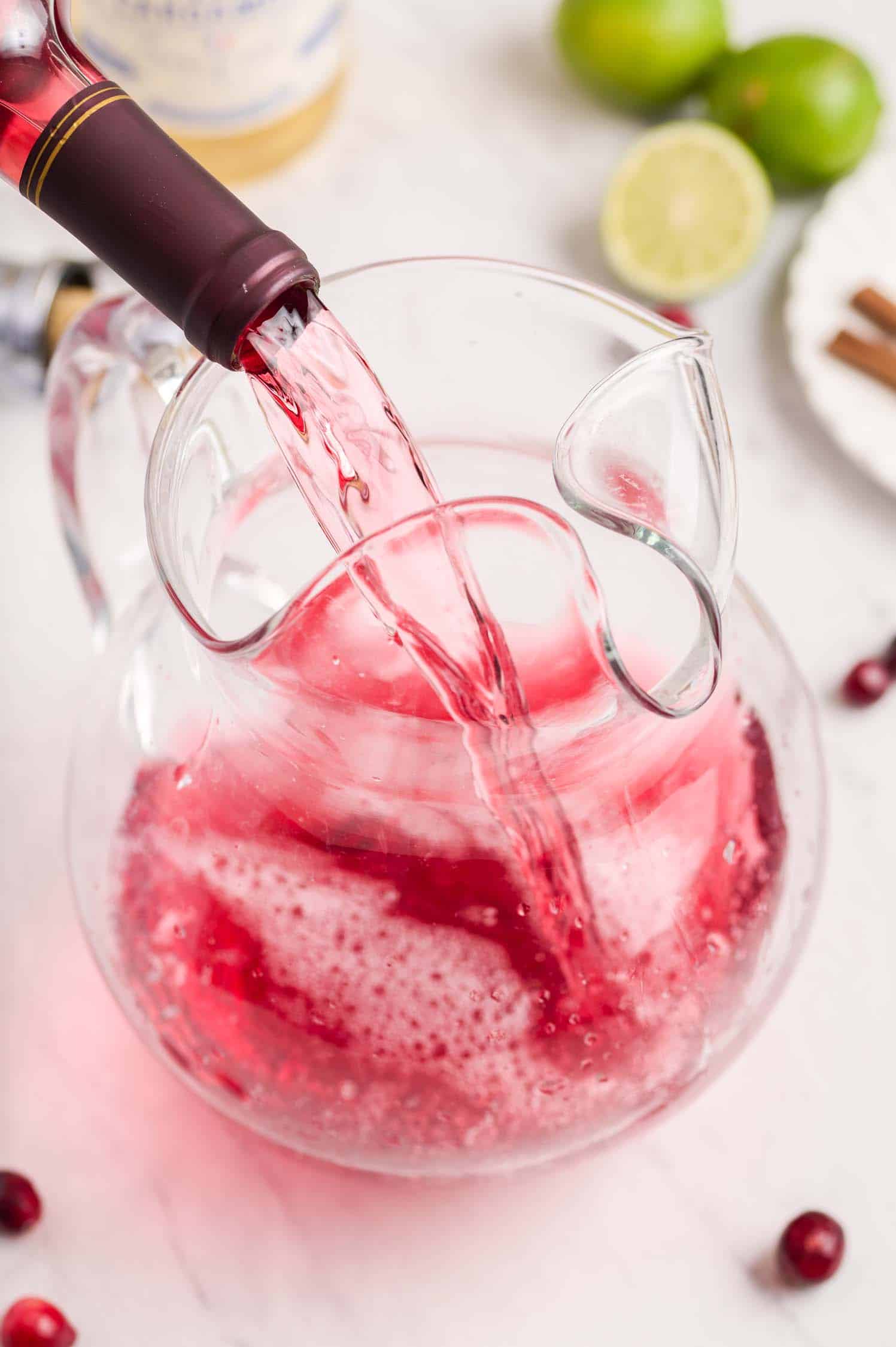 Pouring cranberry wine into a clear glass pitcher