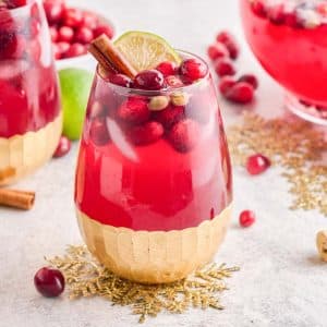 Two glasses of Spiced Cranberry Wine Spritzer in wine glasses on a table with a glass pitcher