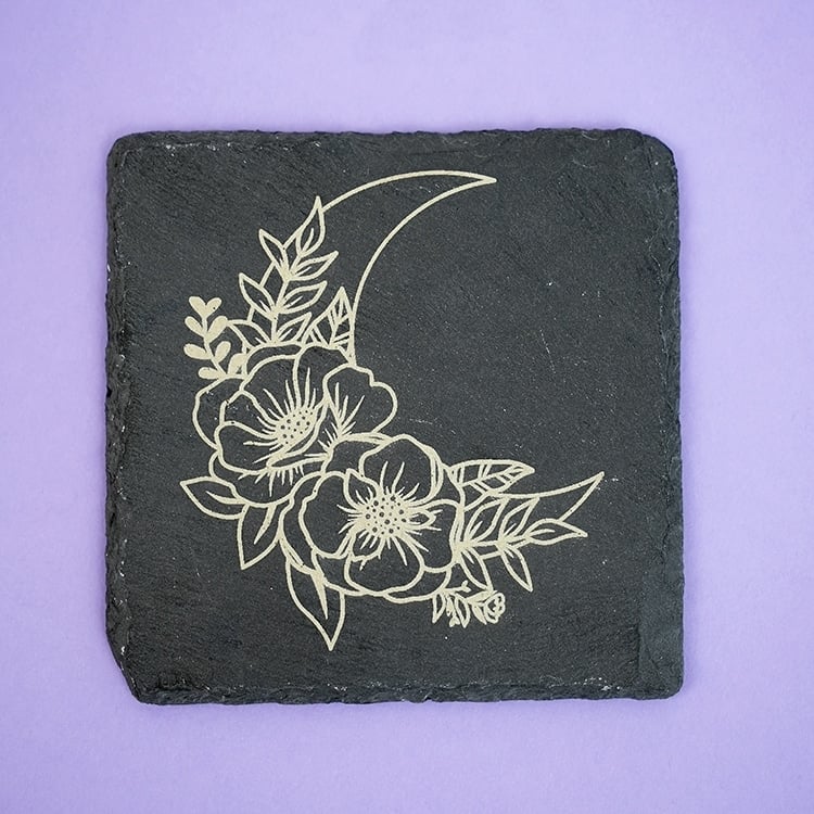 stone coaster engraved with moon and floral design on purple background
