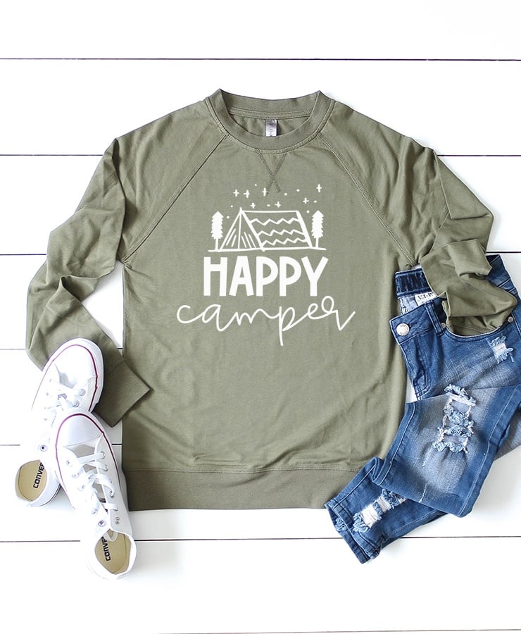 Long sleeved olive green shirt with "Happy Camper" design on white wood background