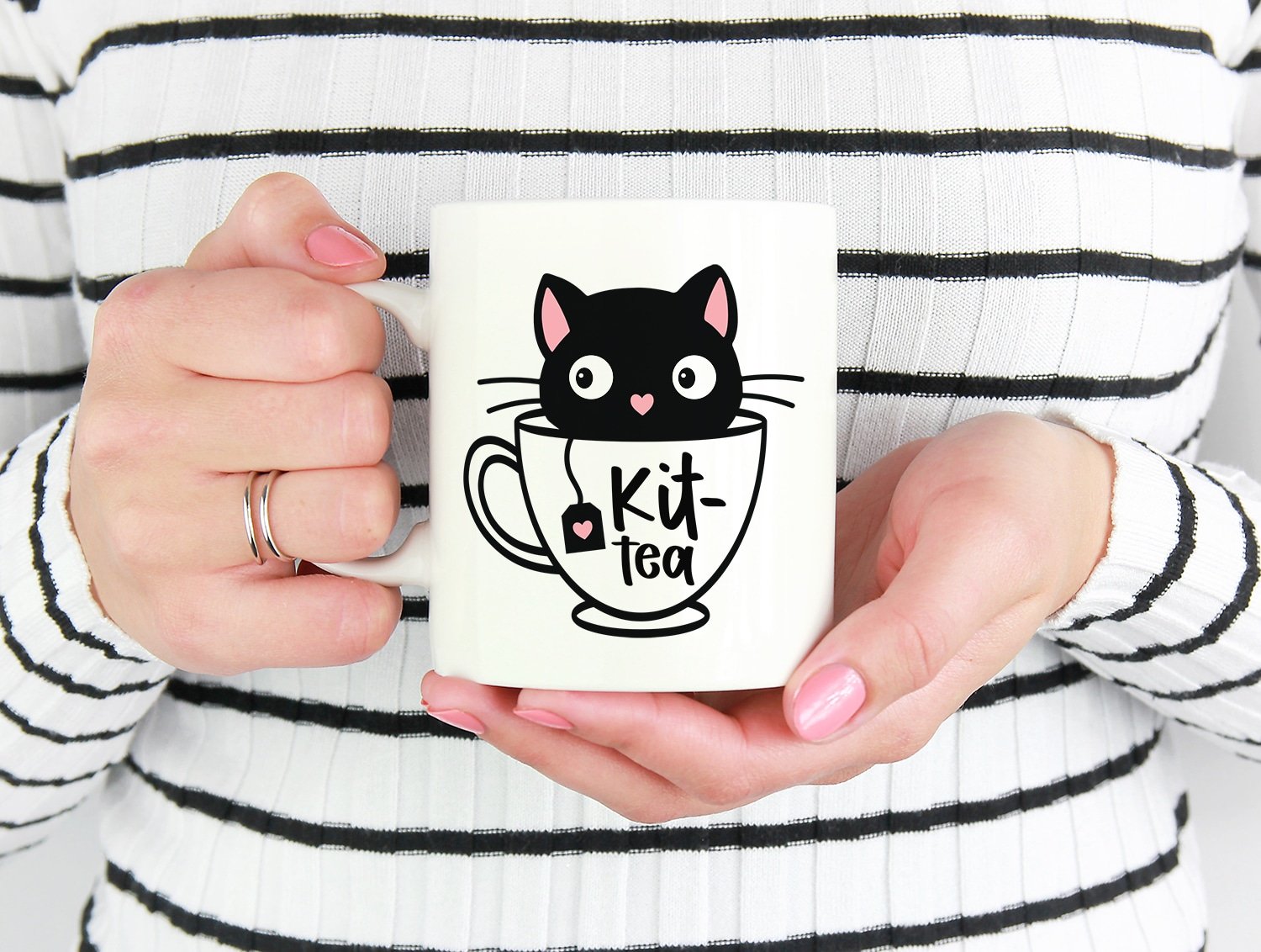 Hands holding a white mug with a "kit-Tea" design featuring a black kitten in a white teacup
