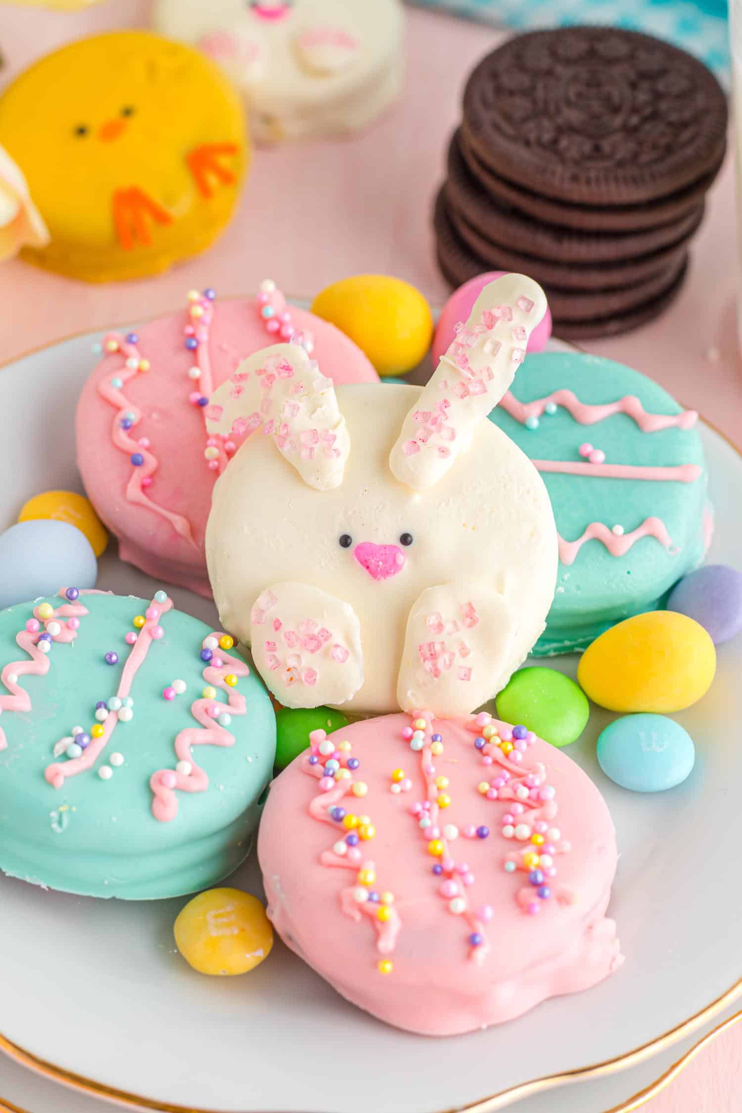 Platter of colorful Easter themed decorated Oreo cookies with a stack of plain Oreo cookies in background