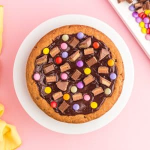 Pastel candies and chocolate chunks added to ganache topping of chocolate chip cookie cake