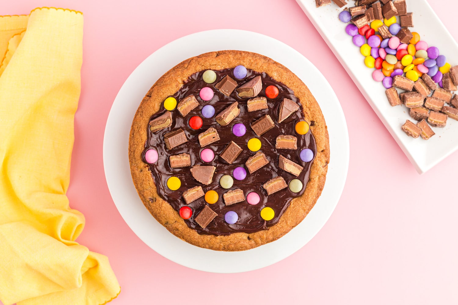 Pastel candies and chocolate chunks added to ganache topping of chocolate chip cookie cake
