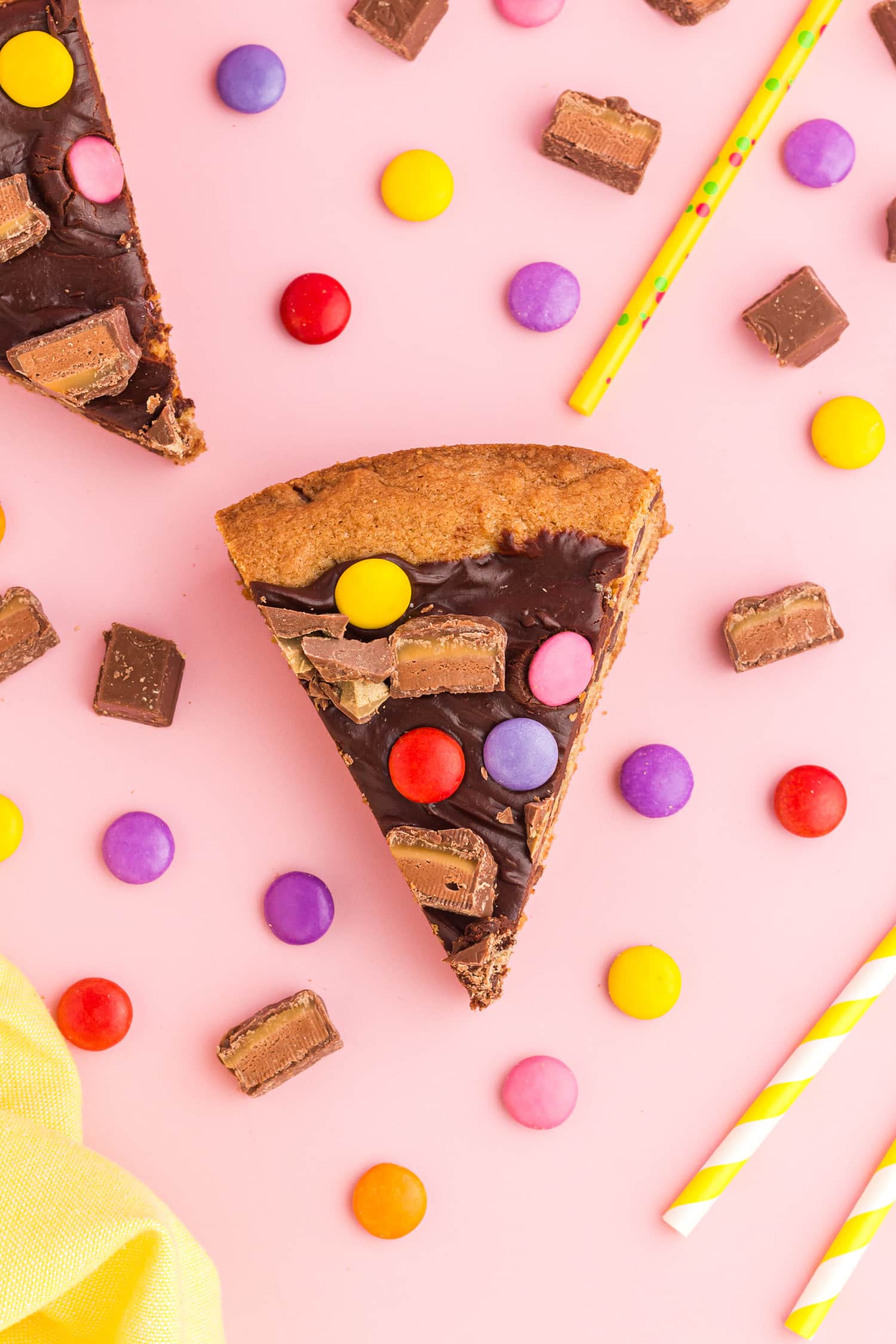 Slice of delicious chocolate chip cookie pizza treat with candy and decorations sprinkled around slice
