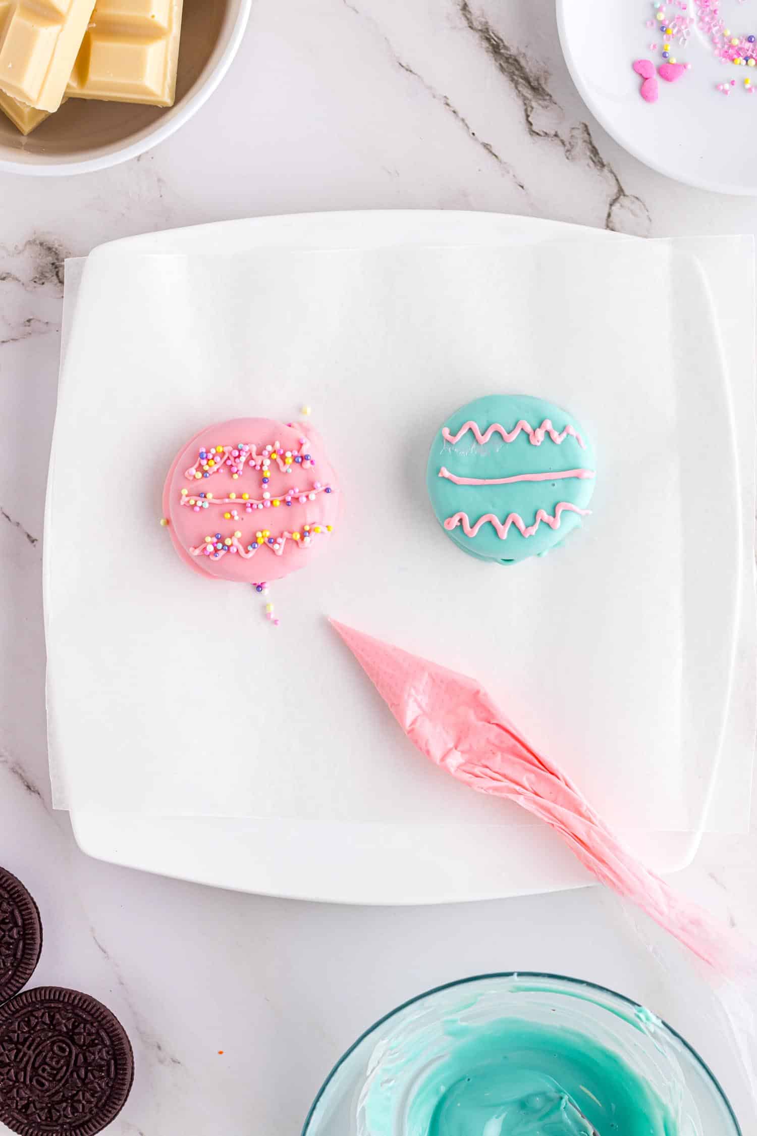 Two chocolate dipped Oreos on plate with emptied piping bag and icing