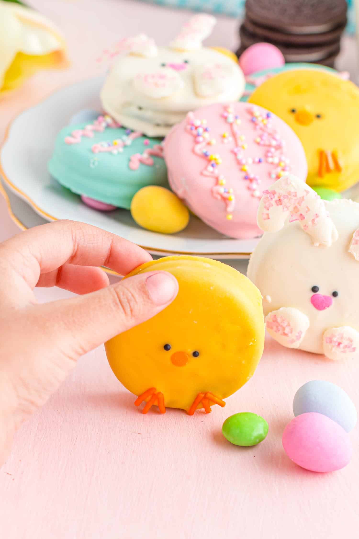 Little hand holding a chocolate covered oreo decorate to look like a chick, plate of cookies in background