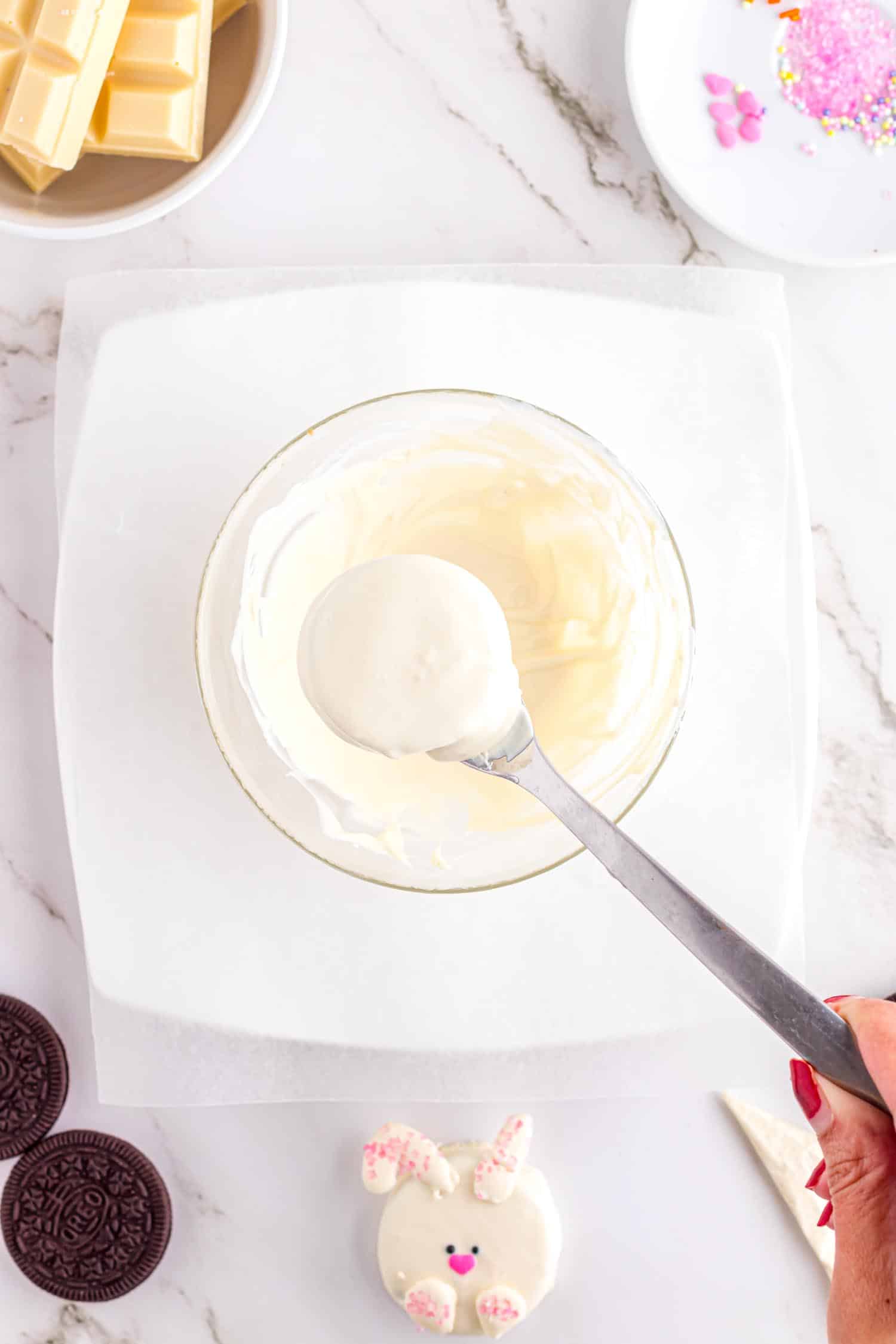 Oreo cookie covered in white chocolate after being dipped into mixing bowl below, held on a fork