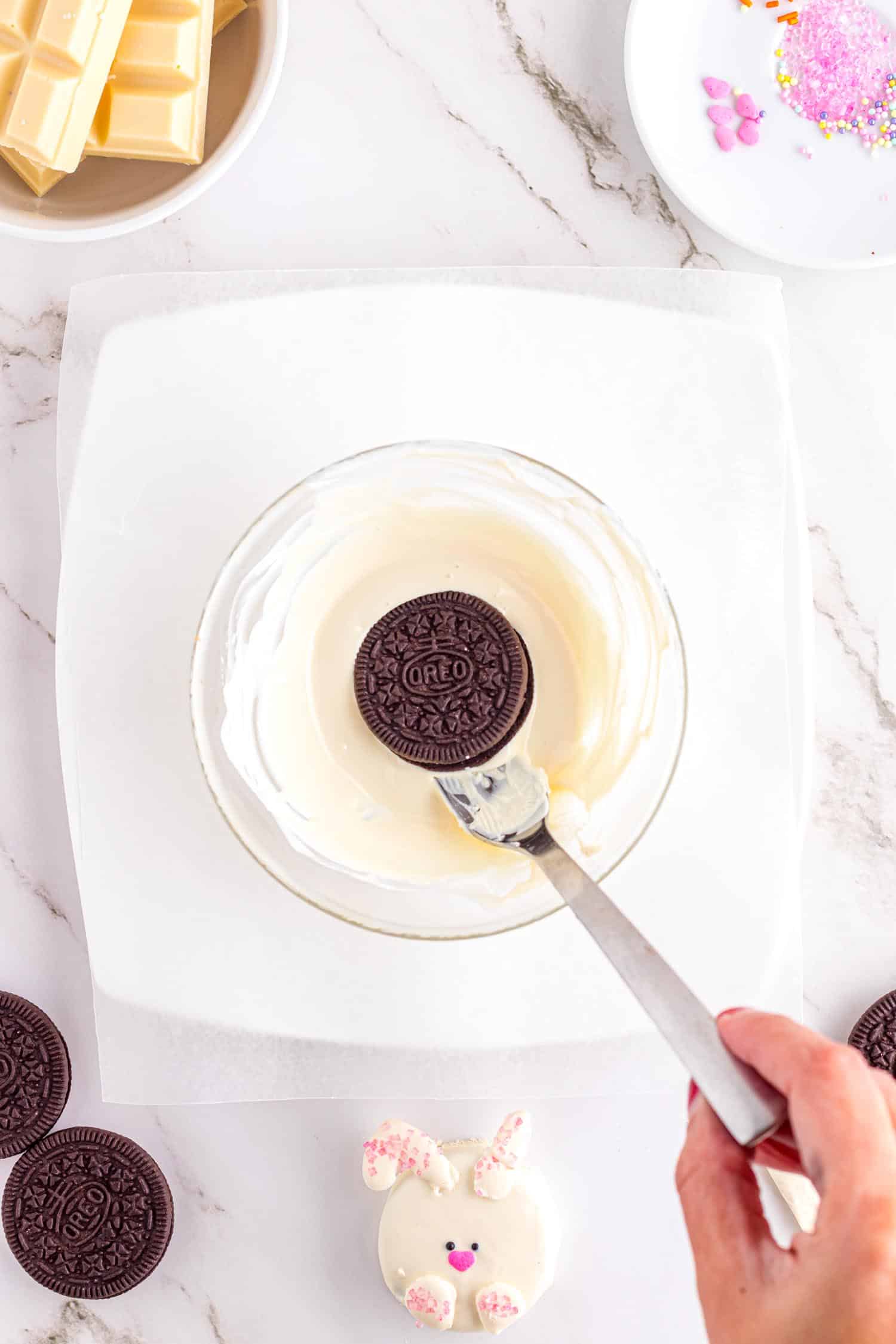 Plain Oreo cookie being lowered on fork into melted white chocolate