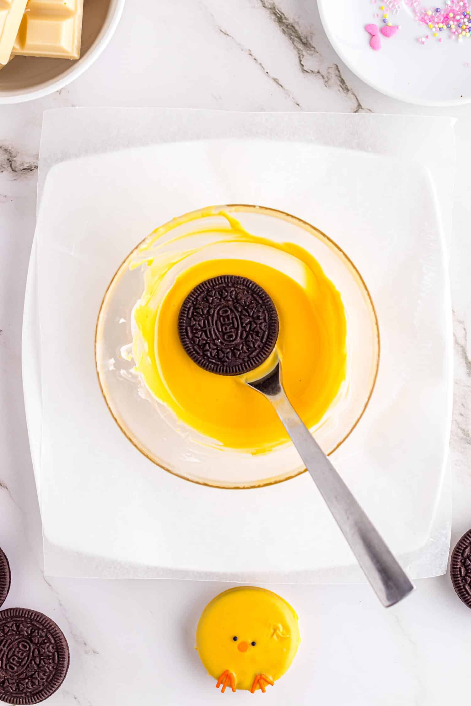 Plain Oreo cookie being lowered on fork into a mixing bowl filled with yellow colored melted chocolate