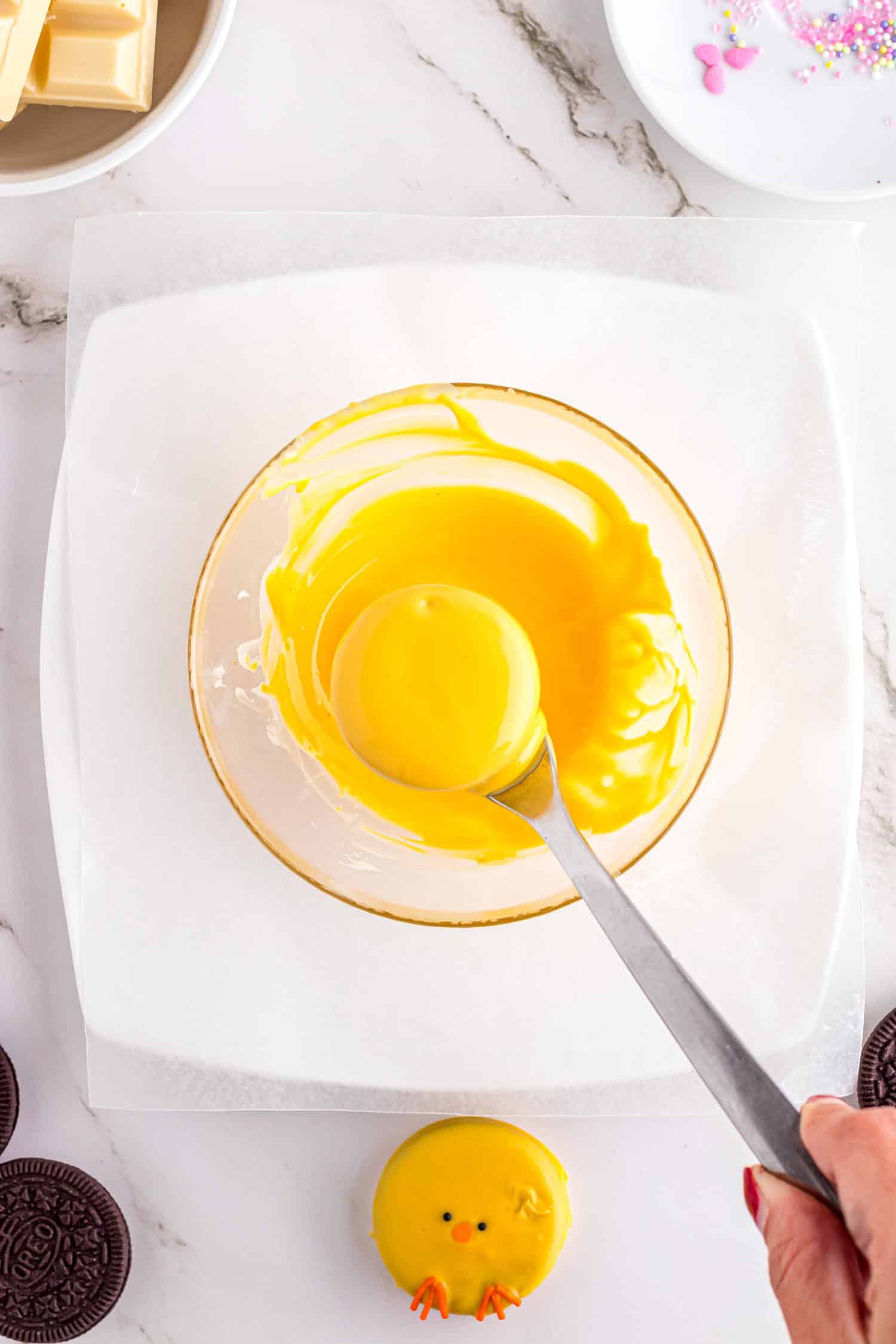 Plain Oreo cookie covered in chocolate after being lowered on fork into a mixing bowl filled with yellow colored melted chocolate