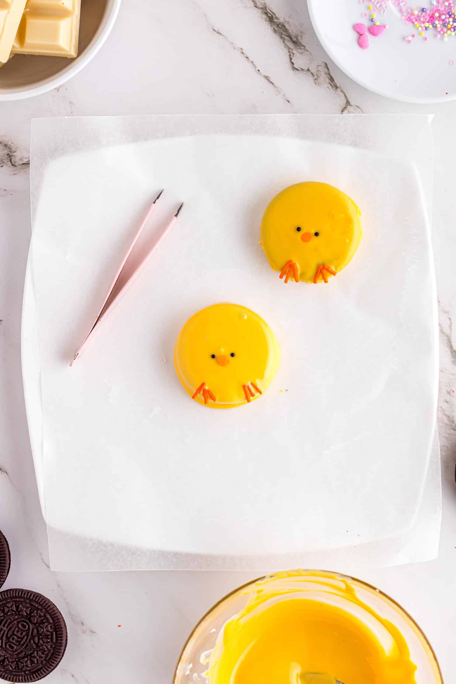 Oreo cookies made to look like tiny chicks sitting on white platter with tweezers placed next to them