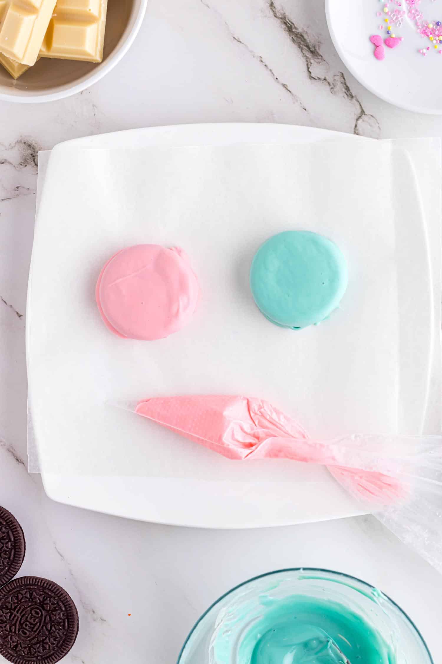 Two Oreo cookies on plate, one pink and one blue after being dipped in melted chocolate