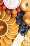 Close up photo that pictures blueberries, strawberries, bagels, waffles, cheese and spreads for party board