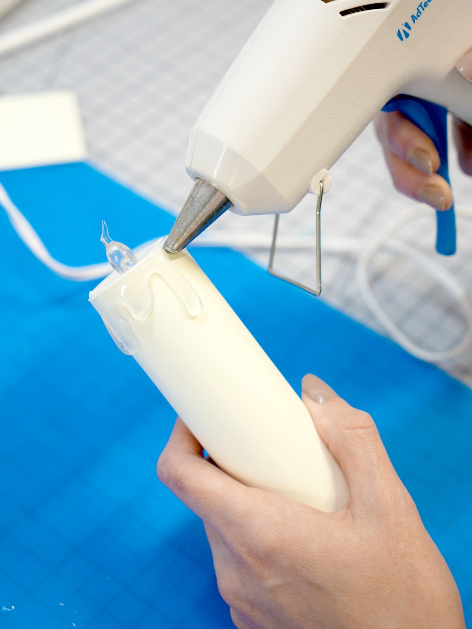 Close up of hands using a hot glue gun to create "wax drips" on a paper candle