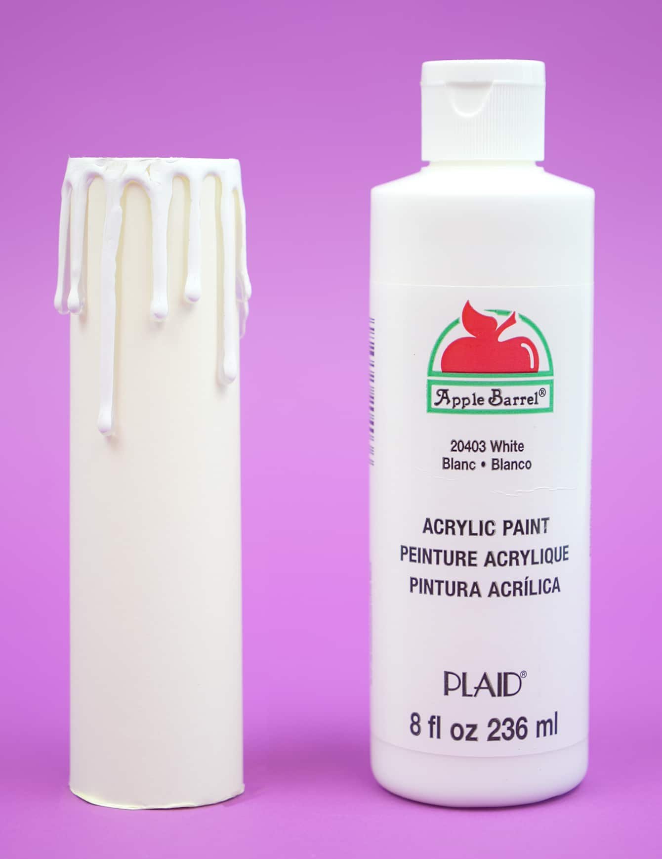 Paper "candle" on a purple background next to a bottle of white paint