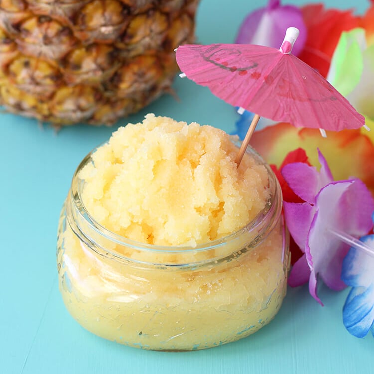 yellow pina colada sugar scrub with a tiki cocktail umbrella on aqua background