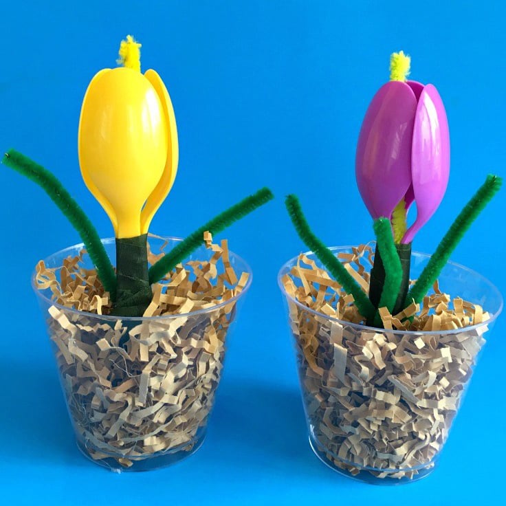 Plastic spoon flowers in cups on blue background