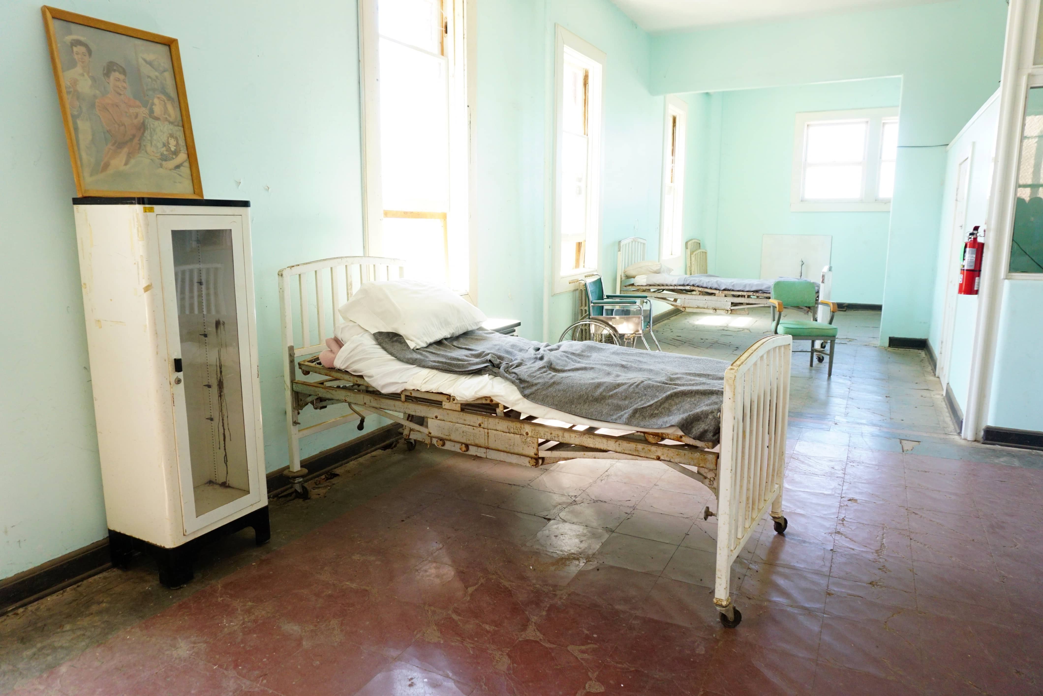 room full of sunlight with mint green walls and antique hospital beds and wheelchair