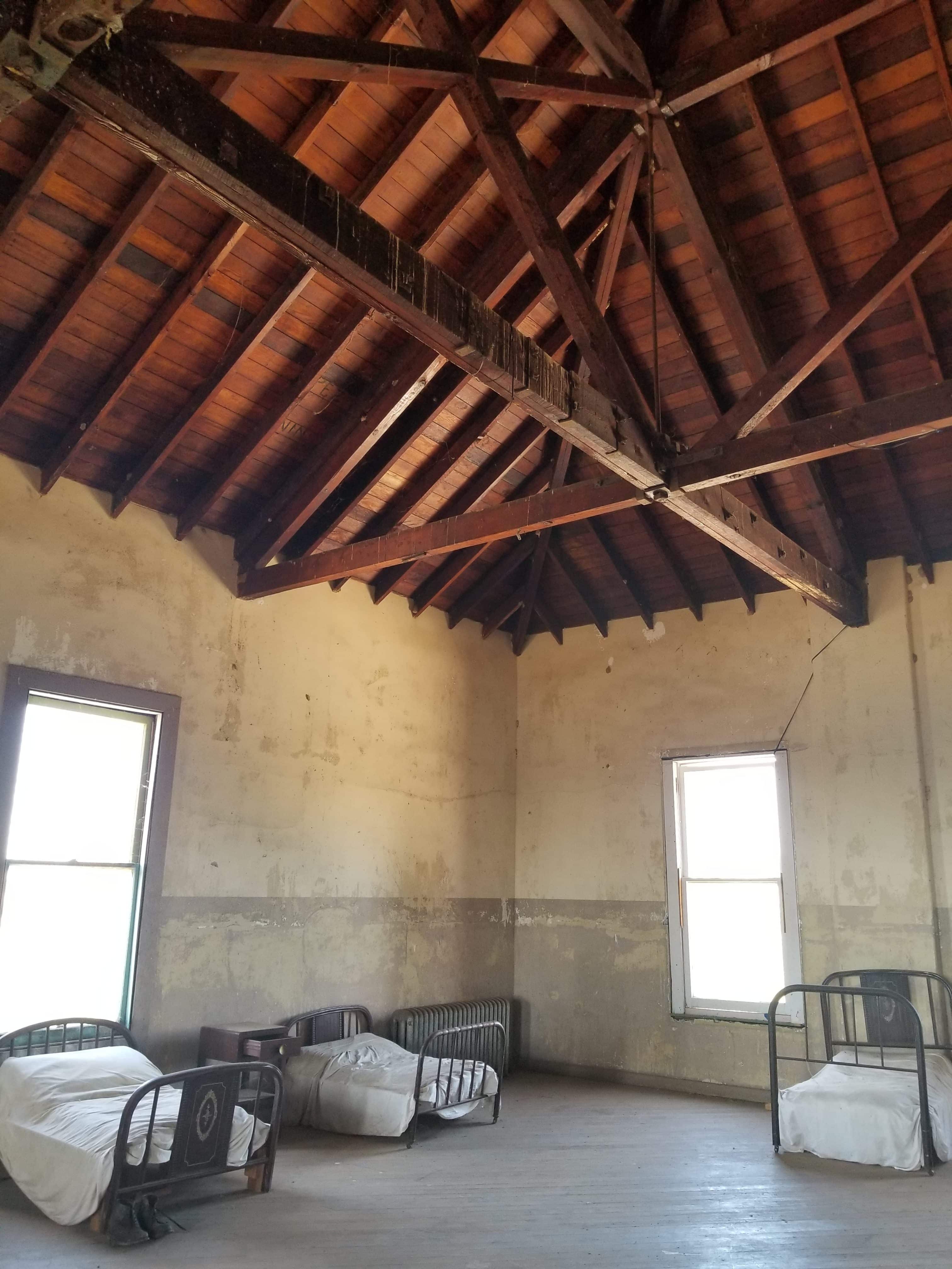 three metal beds in large room with beams and wooden ceiling