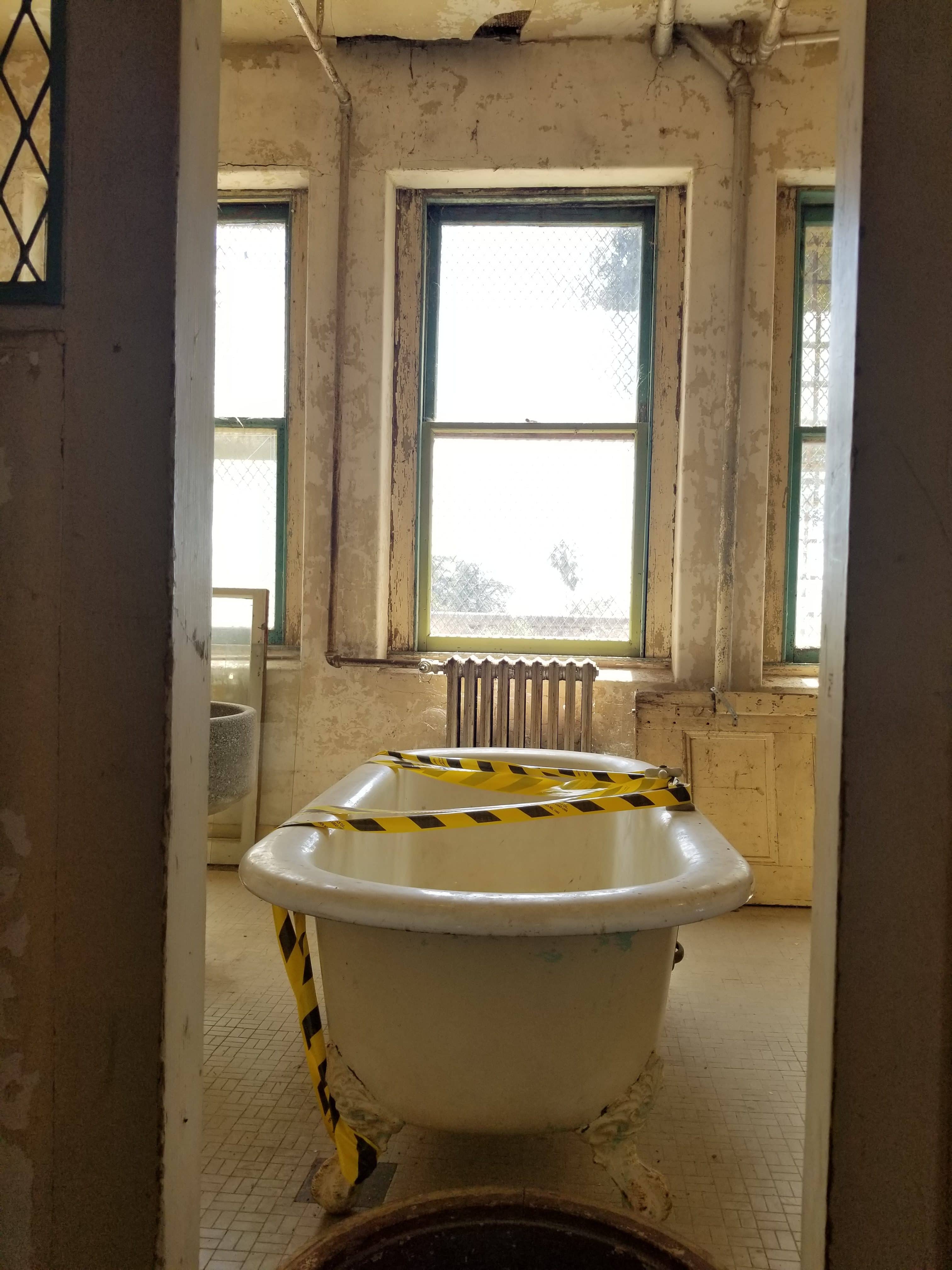 antique claw foot bathtub covered with caution tape in filthy old bathroom