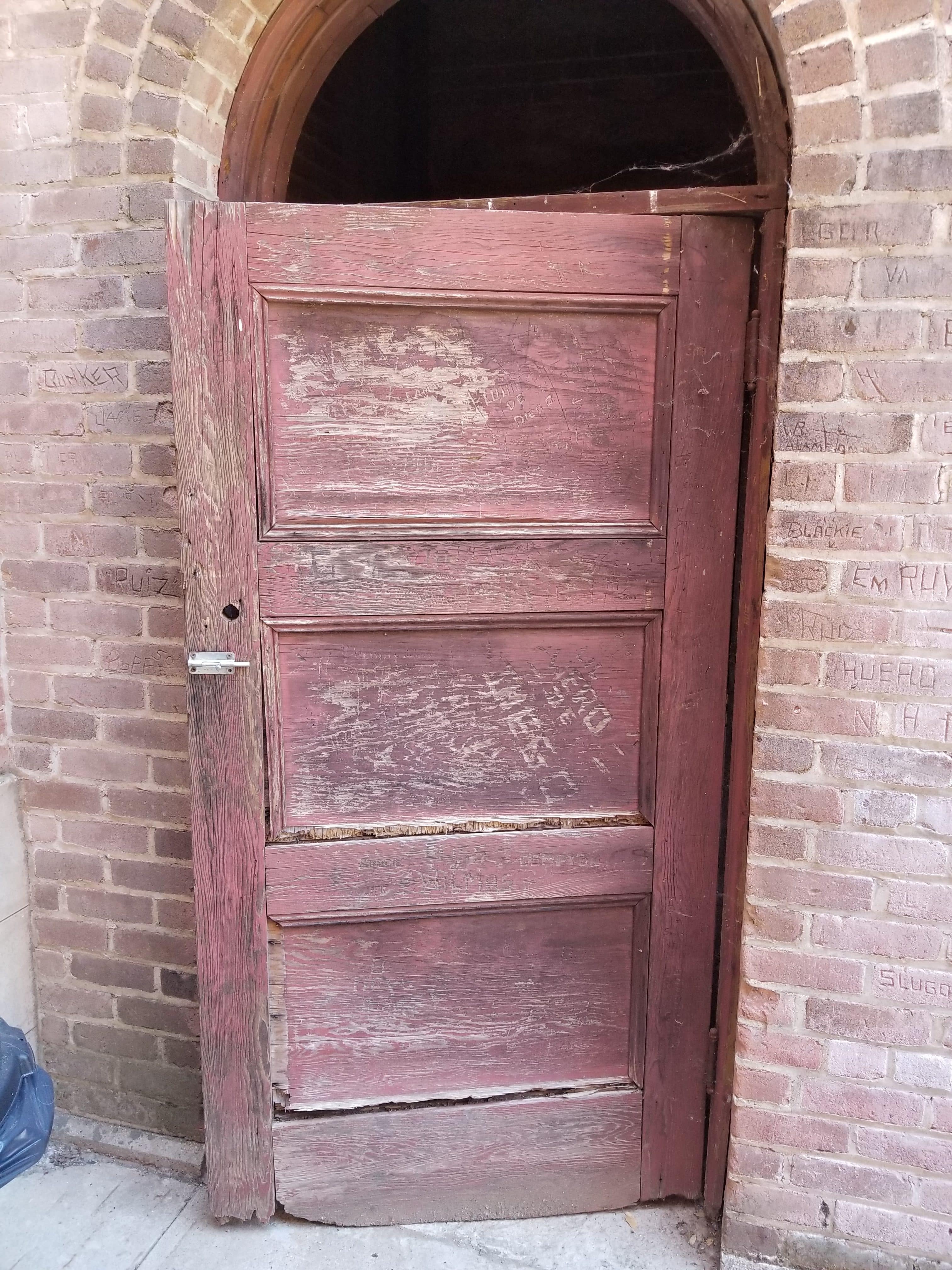 faded and peeling red wooden door in brick wall