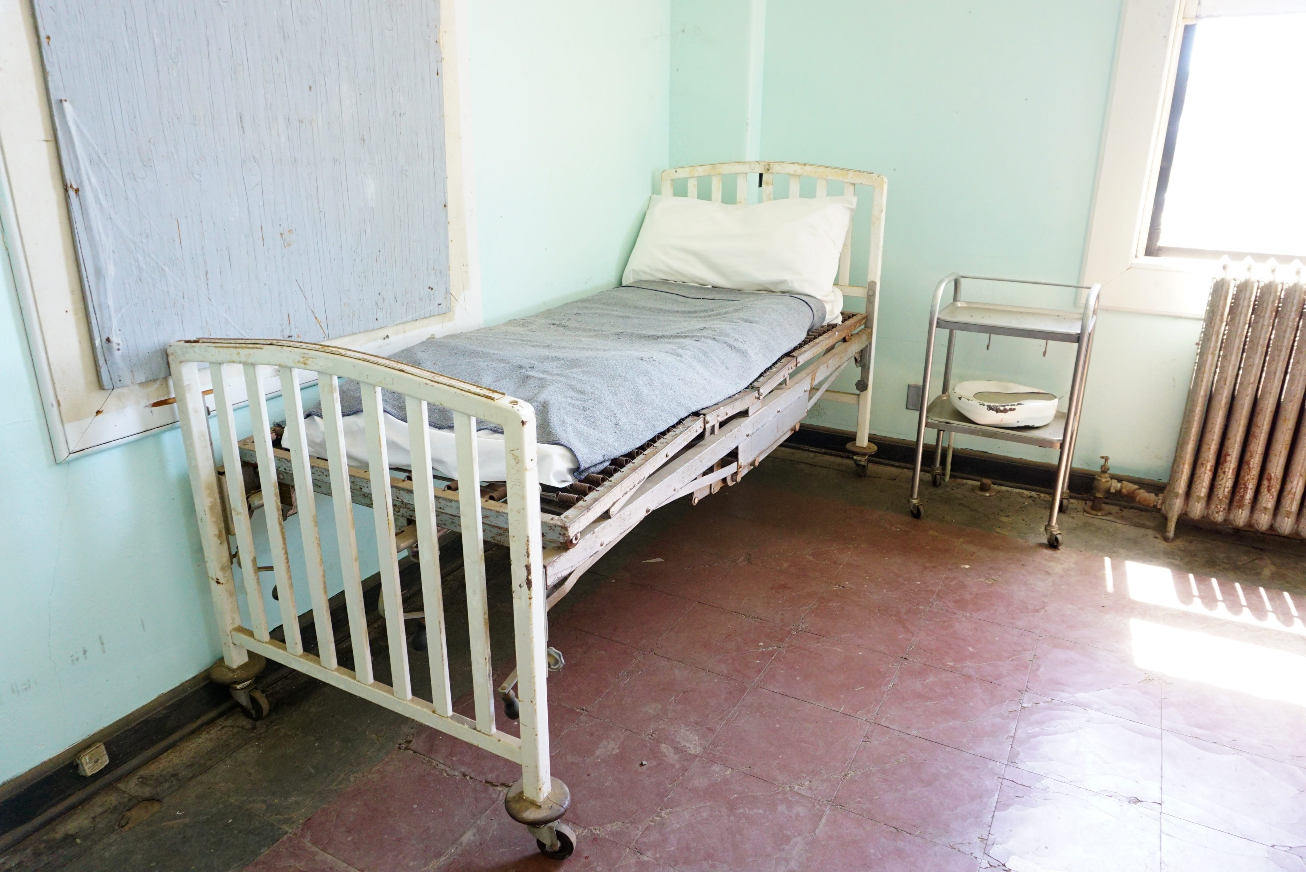 rusty white antique hospital bed with bedpan in sun-filled room