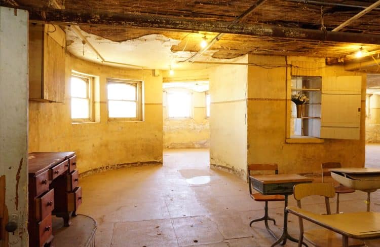dingy and dirty basement room bathed in yellow light with school desks