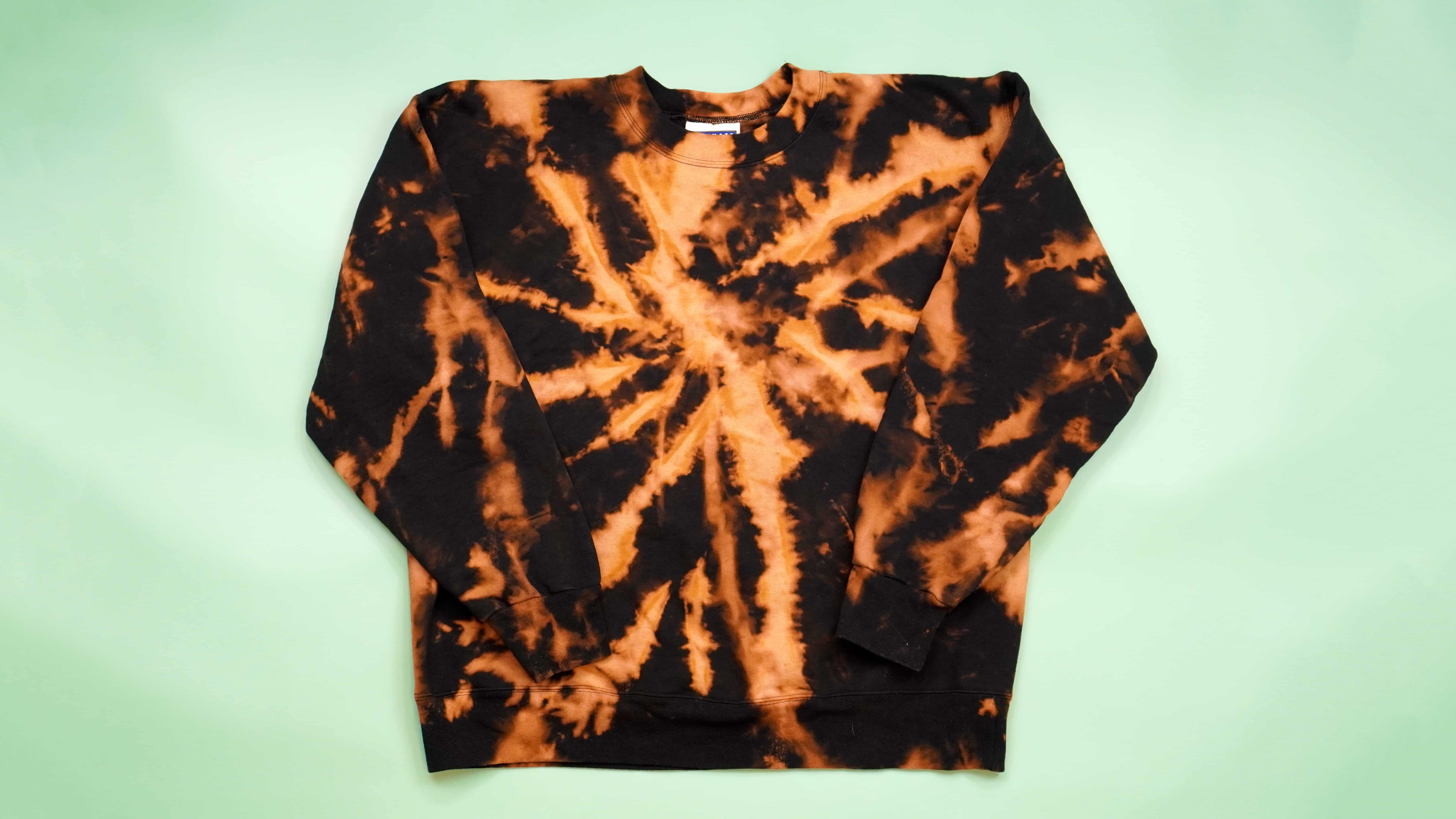 Black and orange bleach tie-dyed sweatshirt on green background