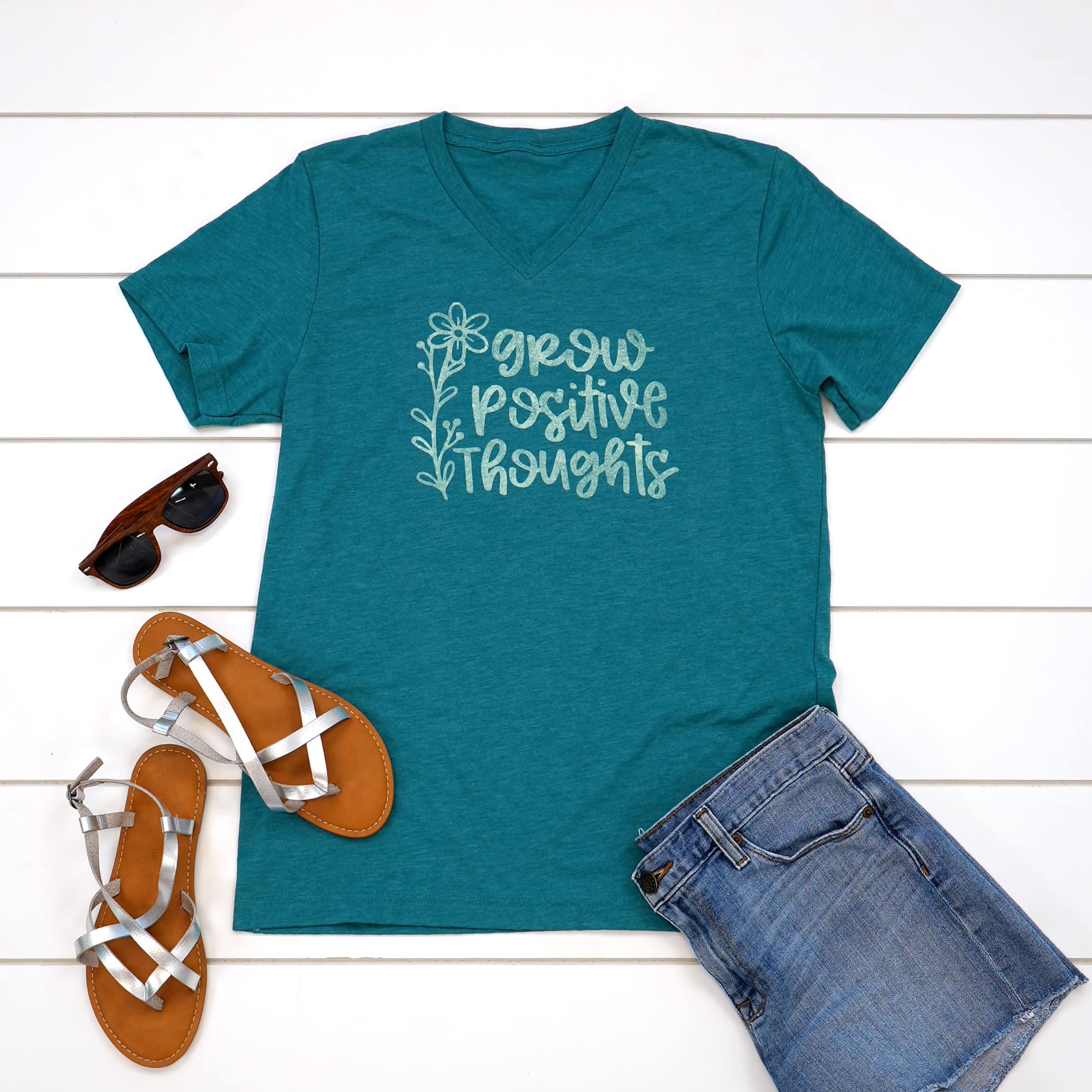 Teal "Grow Positive Thoughts" shirt with outfit in flat lay on white wood background