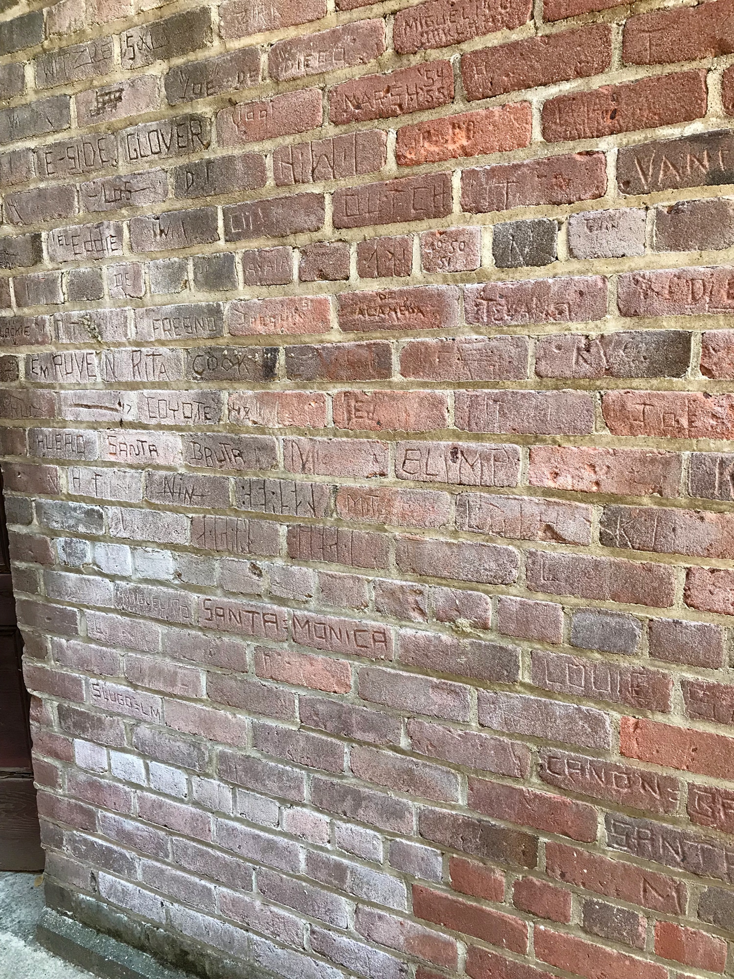 close up of names carved into brick wall in varying shades of red and grey