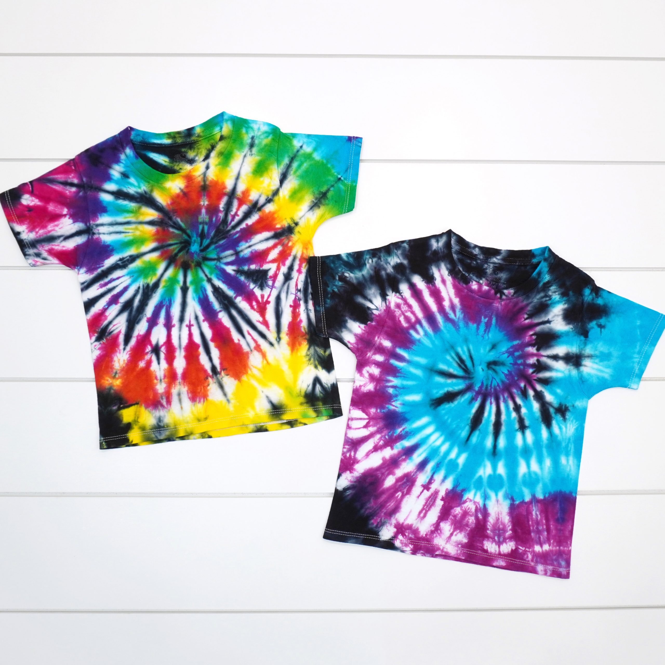 two shirts with colorful spiral tie dye patterns on a white wood background