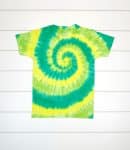 Spiral tie dye pattern shirt in shades of green and yellow on a white wood background