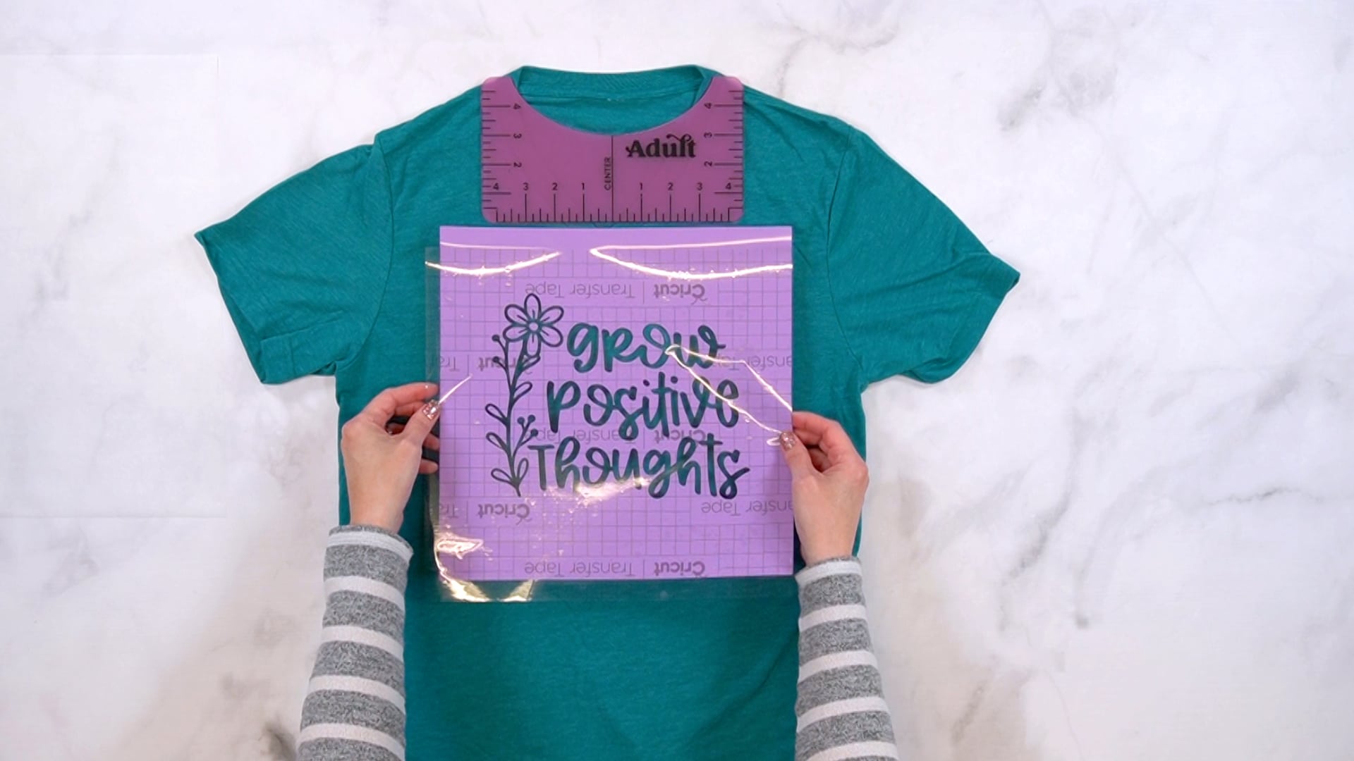 Hands positioning a "Grow Positive Thoughts" design in purple vinyl onto shirt
