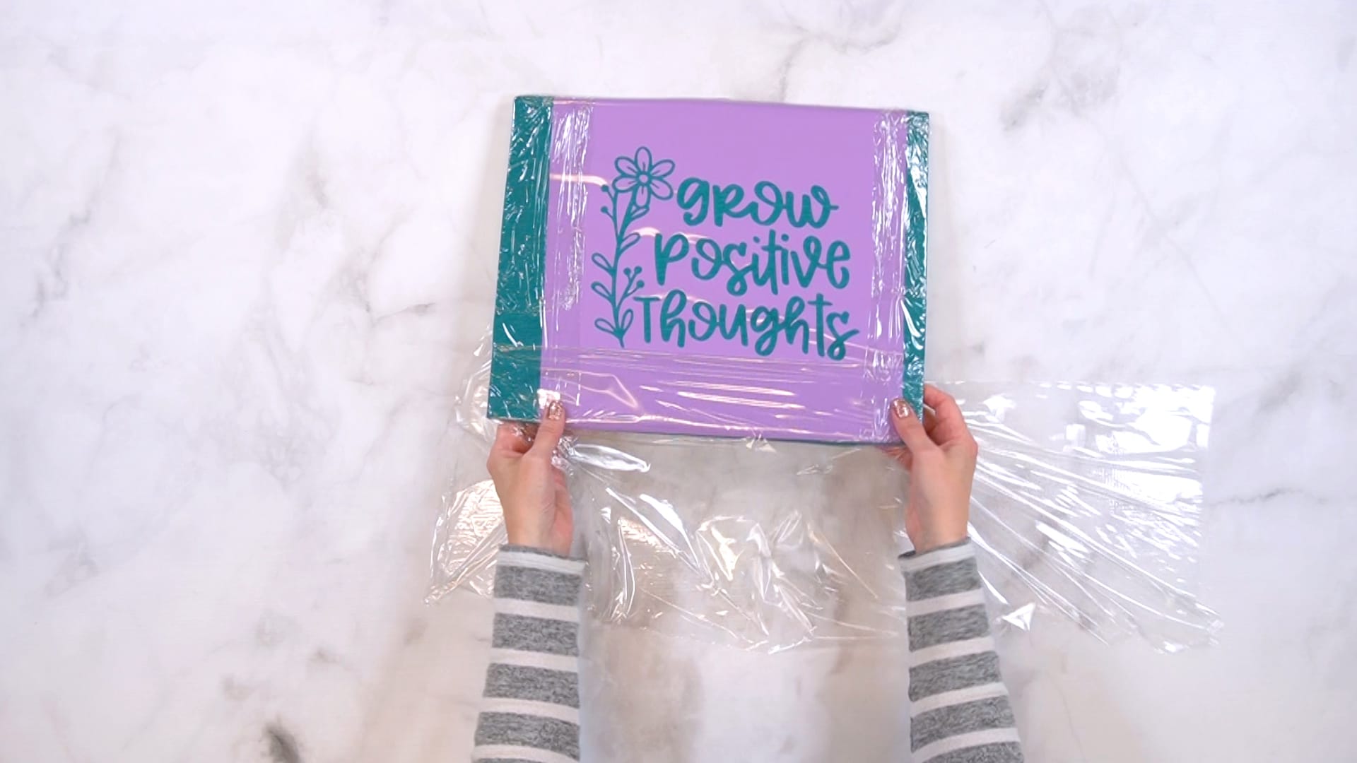 Hands wrapping the edges of a folded and stencil-covered shirt in plastic wrap