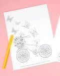 Bicycle with basket of flowers and butterflies coloring sheet on a pink background