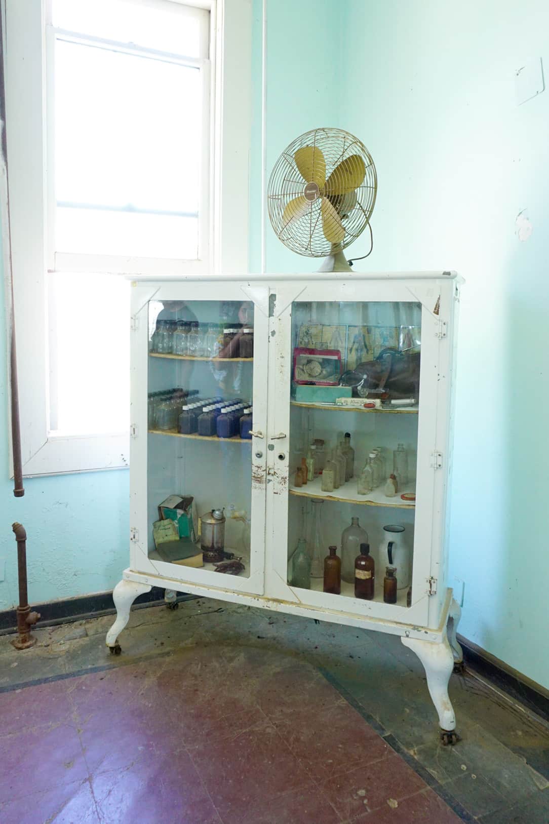 rusty white apothecary cabinet filled with different colored bottles