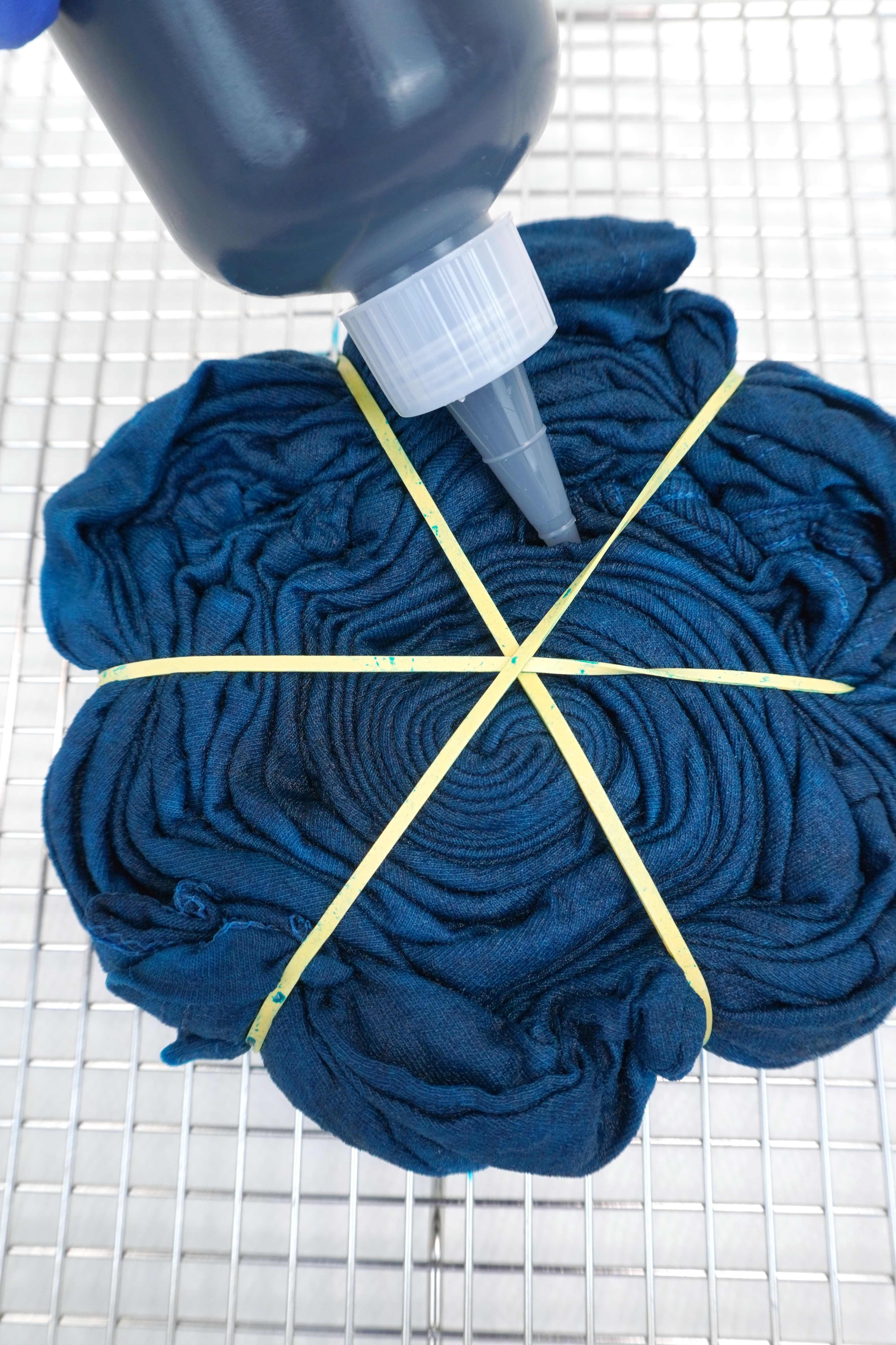 Close up of bottle applying dark teal blue dye to a spiral folded tie-dye shirt