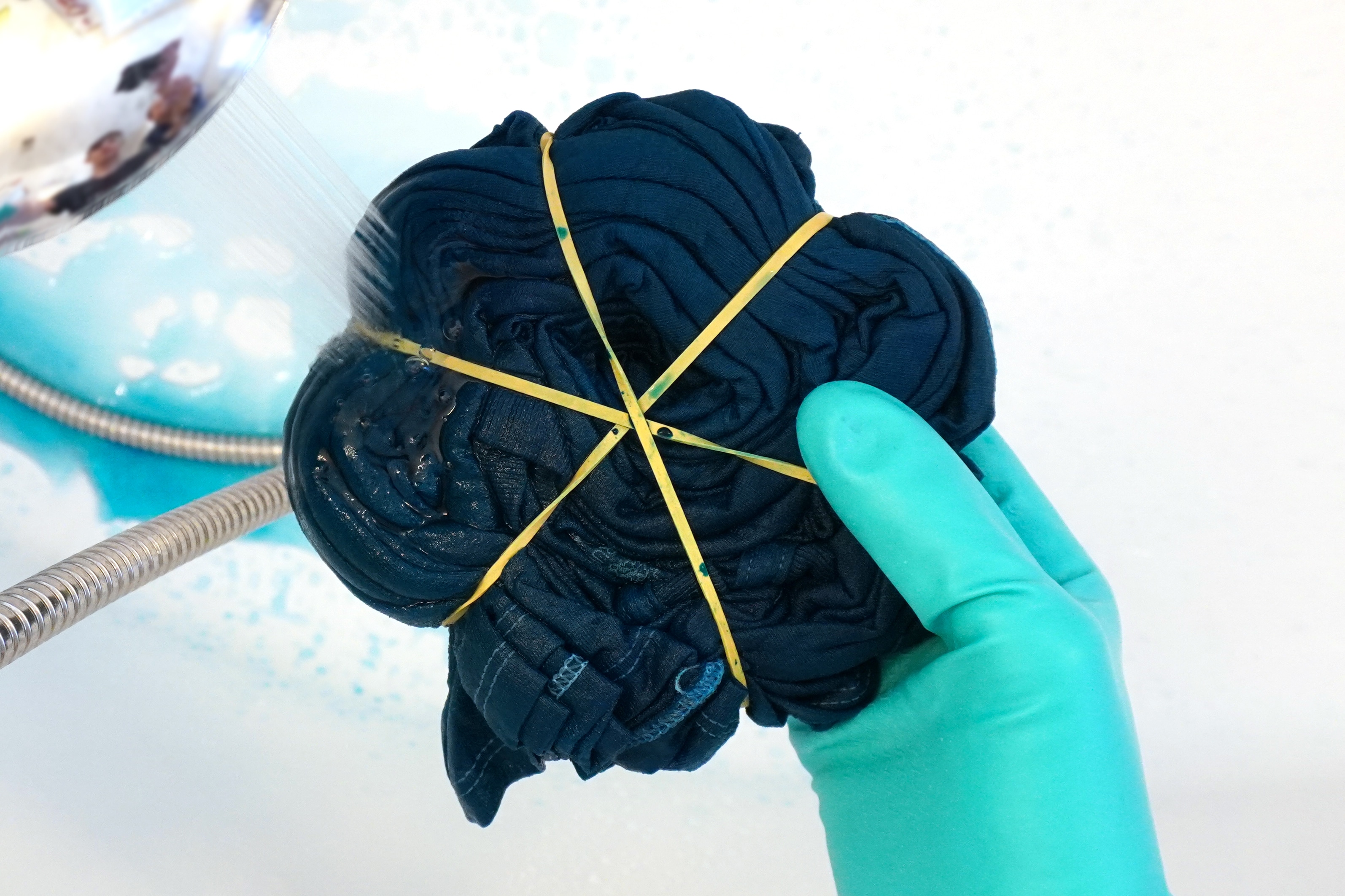 Close up of gloved hand holding and rinsing a folded spiral tie-dye shirt