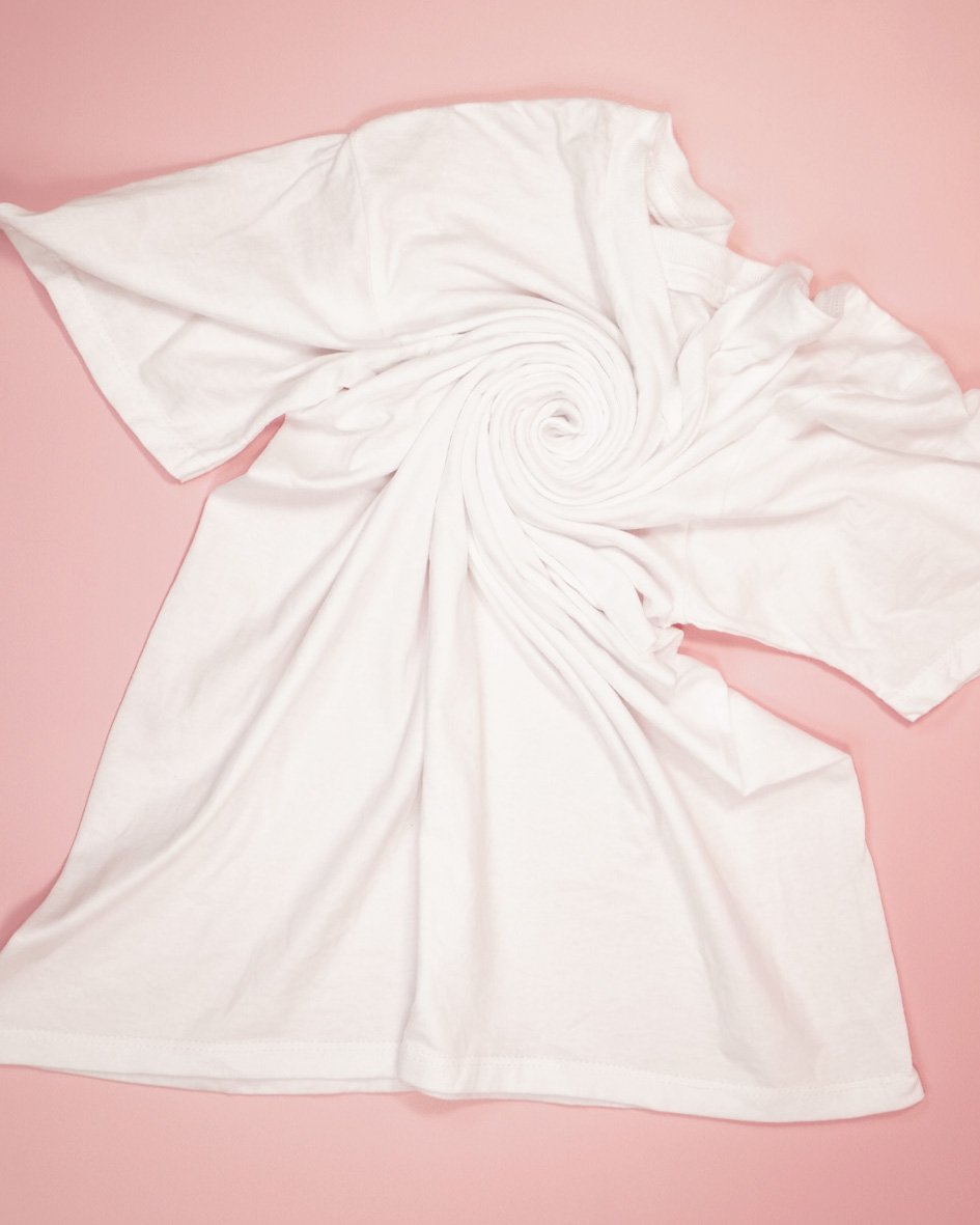 spiral tie dye folding in progress on white shirt on pink background
