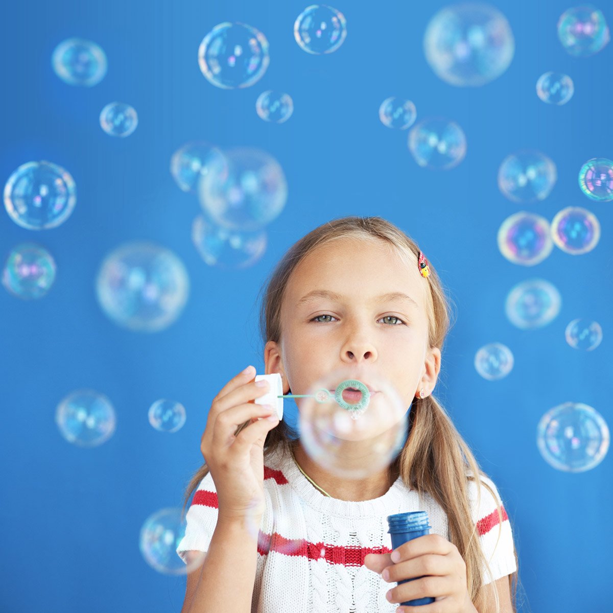 Portrait of blonde haired little girl blowing bubbles on a blue background