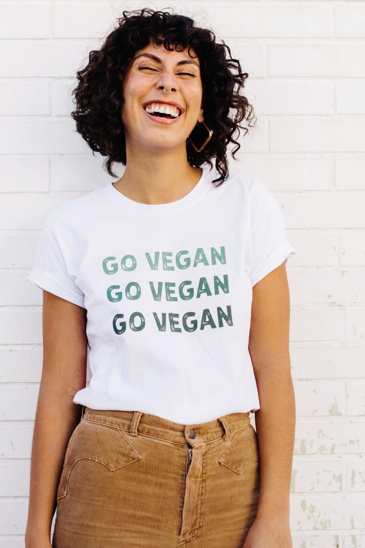 Happy young woman laughing cheerfully while wearing a shirt with the words "GO VEGAN" written on it.