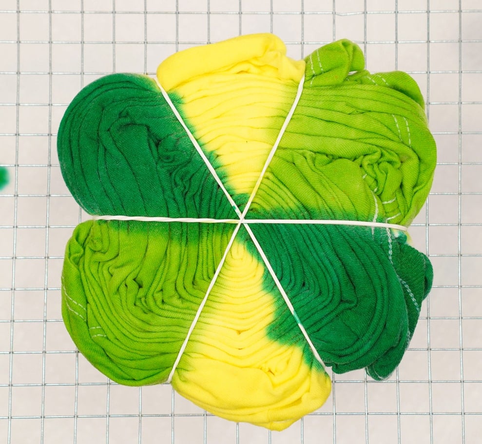 spiral tie-dye folded shirt on a wire rack with green and yellow dye applied