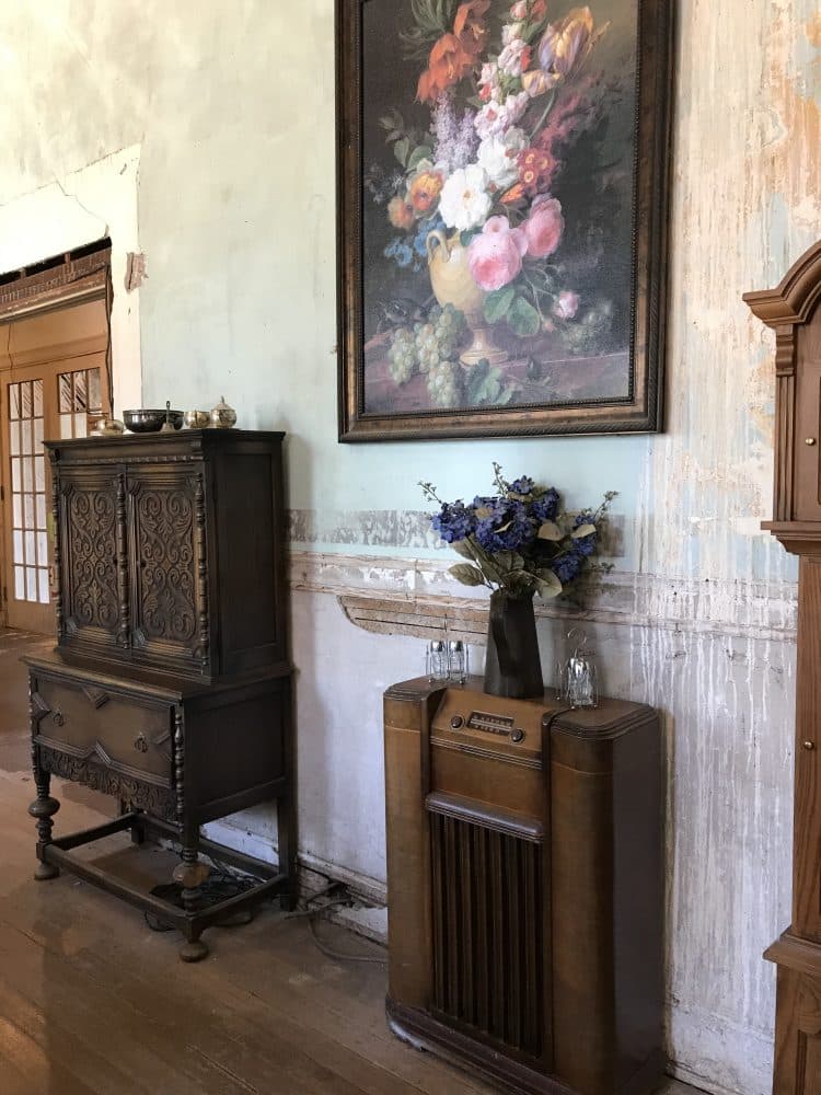 Ornately carved wood chest, antique console radio, and floral oil painting in dining room